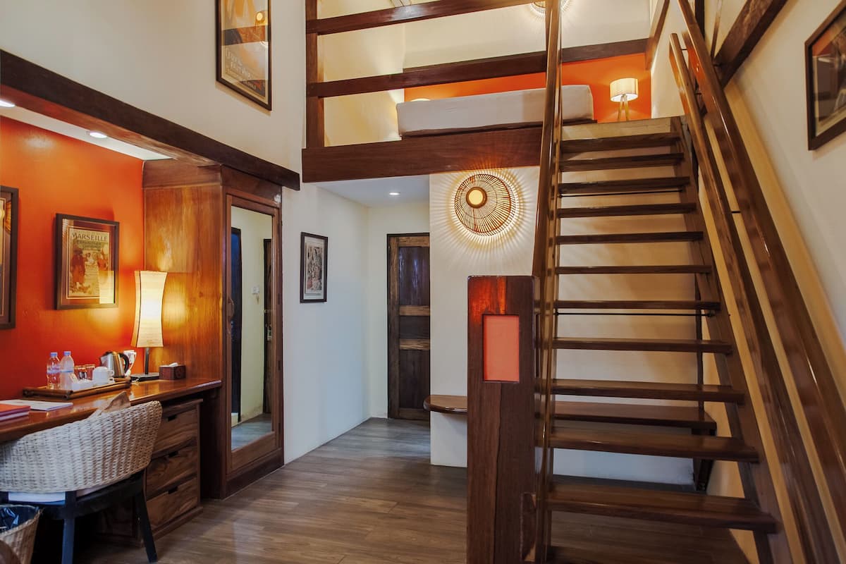 A hotel lobby with a wooden staircase, a desk with a lamp, and framed pictures on the walls.