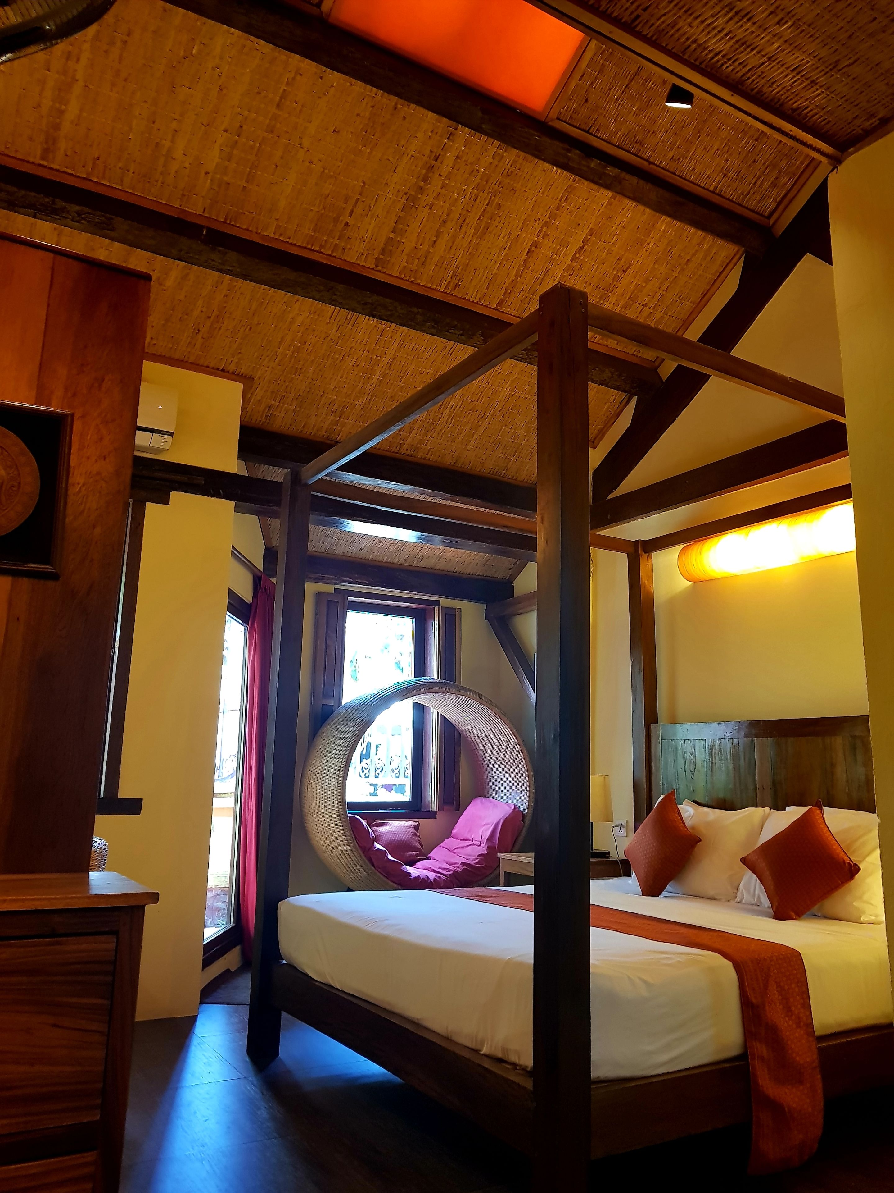 A room with a bed, a hanging chair, and a window with curtains.