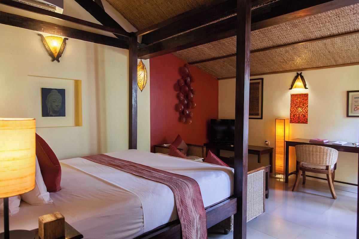 A room with a bed, a desk, and a chair. There are wall sconces and a wall-mounted lamp.