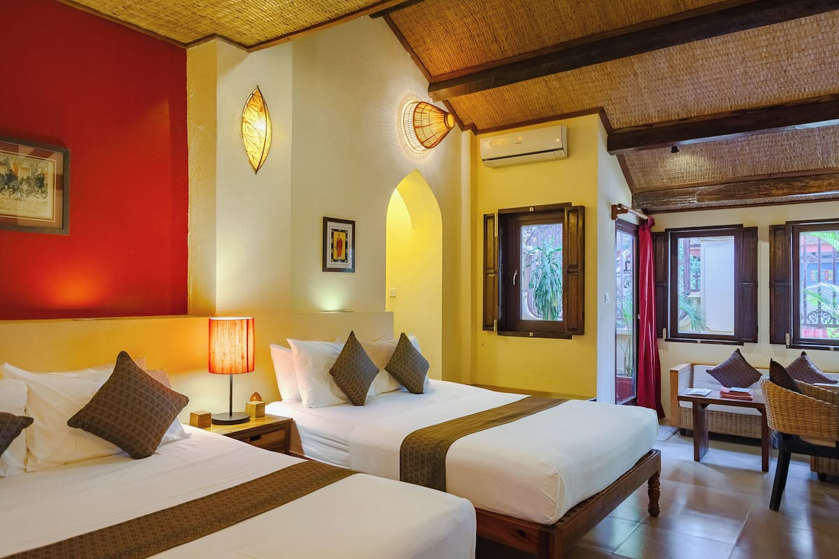 A hotel room with two beds, a wooden ceiling, and a view of greenery outside.
