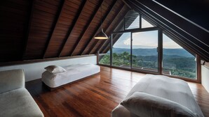 Una habitación con techos altos y techo inclinado, un ventanal con vistas al paisaje y una cama con un almohadón.