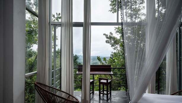 Una habitación con ventanas amplias, una mesa de madera y una silla de mimbre.