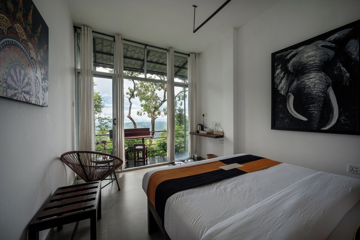 A bedroom with a large bed, a chair, a bench, a window with a view, and a painting of an elephant.