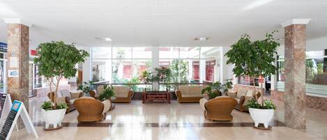 A spacious lobby with a high ceiling, large windows, and several potted plants.