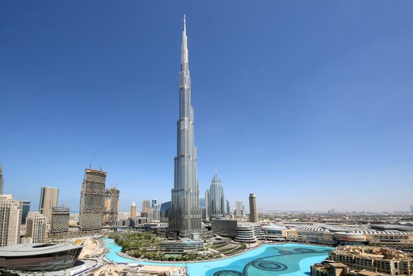 A high-rise building with a distinctive spire, surrounded by other modern skyscrapers and a large, curved water feature.