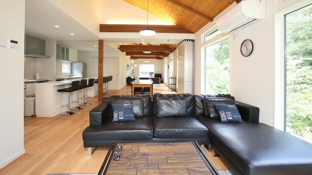 A modern living room with a sectional sofa, a dining area, and a kitchen in the background. - Salji (Hakuba)
