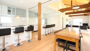 A modern kitchen with white cabinets, a wooden ceiling, and a long dining table with bar stools. - Salji (Hakuba)