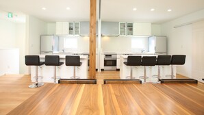 A modern kitchen with white cabinets, stainless steel appliances, and a central wooden column. - Salji (Hakuba)
