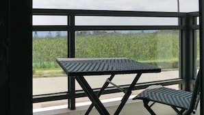 Un balcón con dos sillas de metal negro y una mesa, con vista a una calle y follaje.