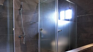 Un box de ducha moderno con puerta de cristal, cabezal de ducha de mano y grifo empotrado.
