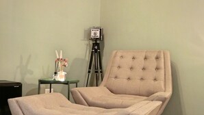 Una habitación con un chaise lounge tapizado, una cámara montada sobre un trípode y obras de arte enmarcadas en la pared.