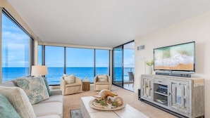A modern living room with a large TV, comfortable seating, and a view of the ocean. - Tranquil OceanFront 2BD AC Pool, Amazing Views - Mahana 519 (Lahaina)