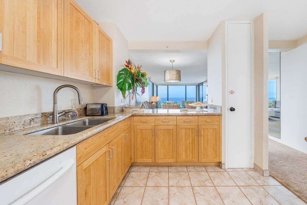 A kitchen with wooden cabinets, a granite countertop, and a view of the ocean through large windows.