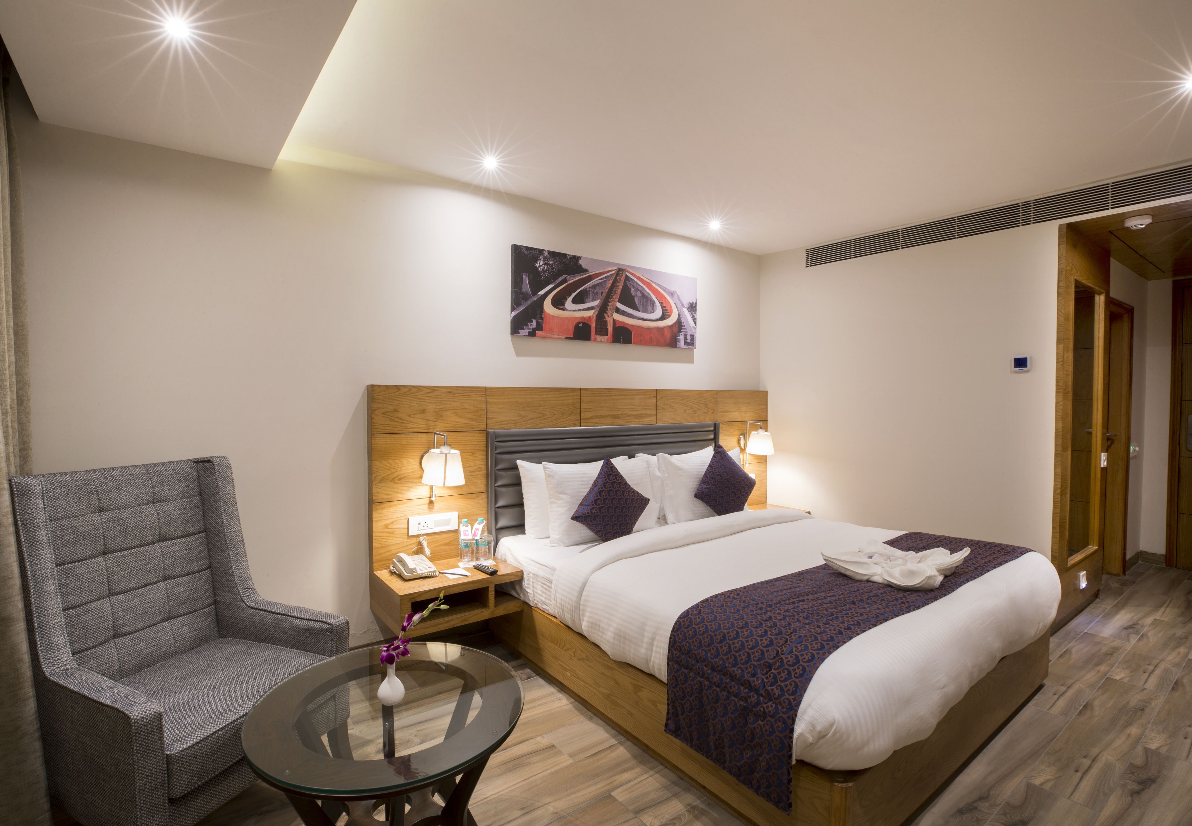 Habitación de hotel con una cama, una silla, una mesita de noche y una obra de arte en la pared.