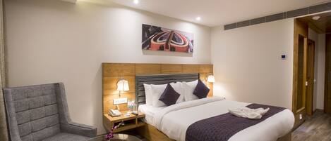 Habitación de hotel con una cama, una silla, una mesita de noche y una obra de arte en la pared.
