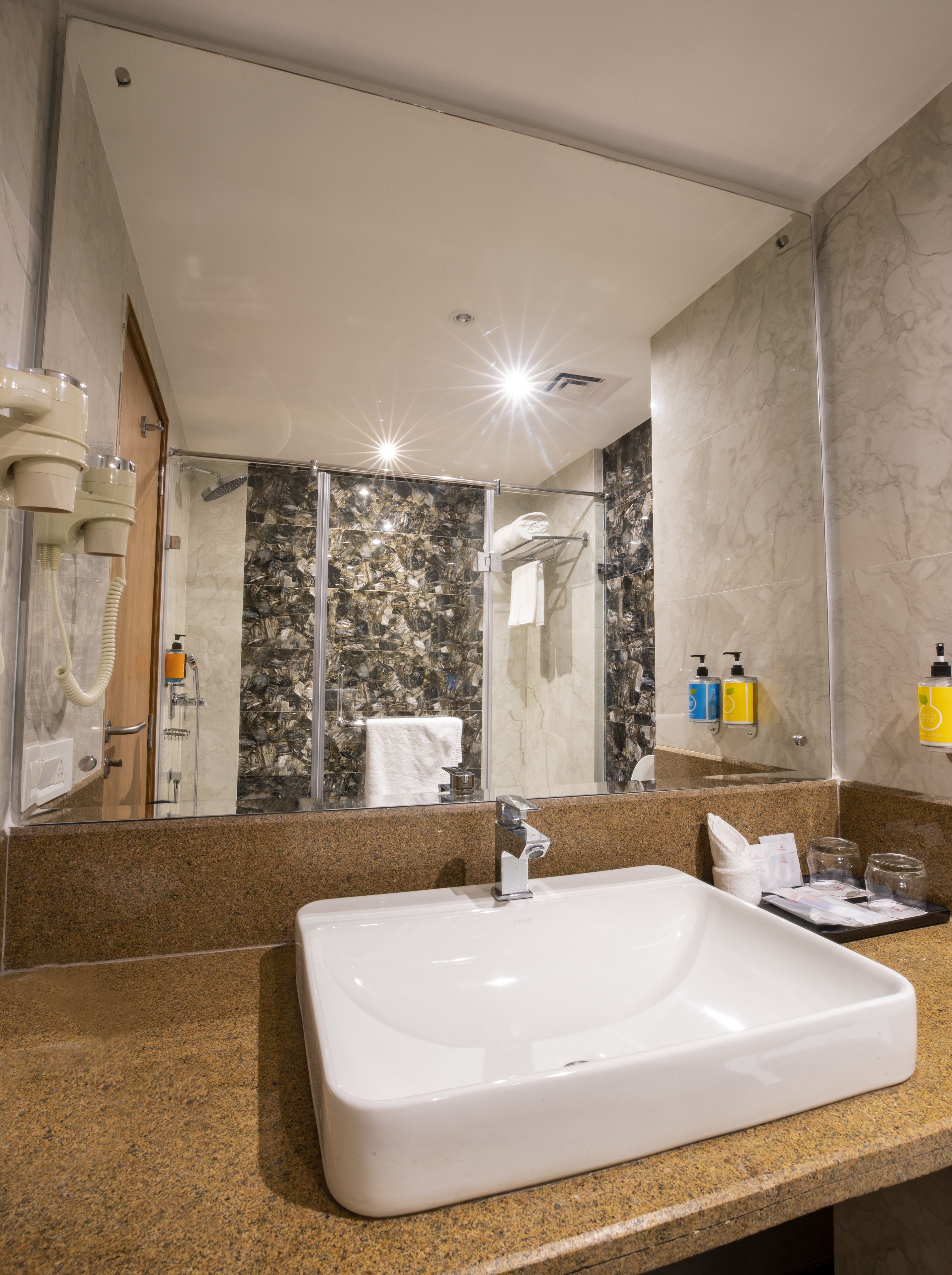 A bathroom with a large white sink, a glass-enclosed shower, marble walls, and a mirror reflecting the room.