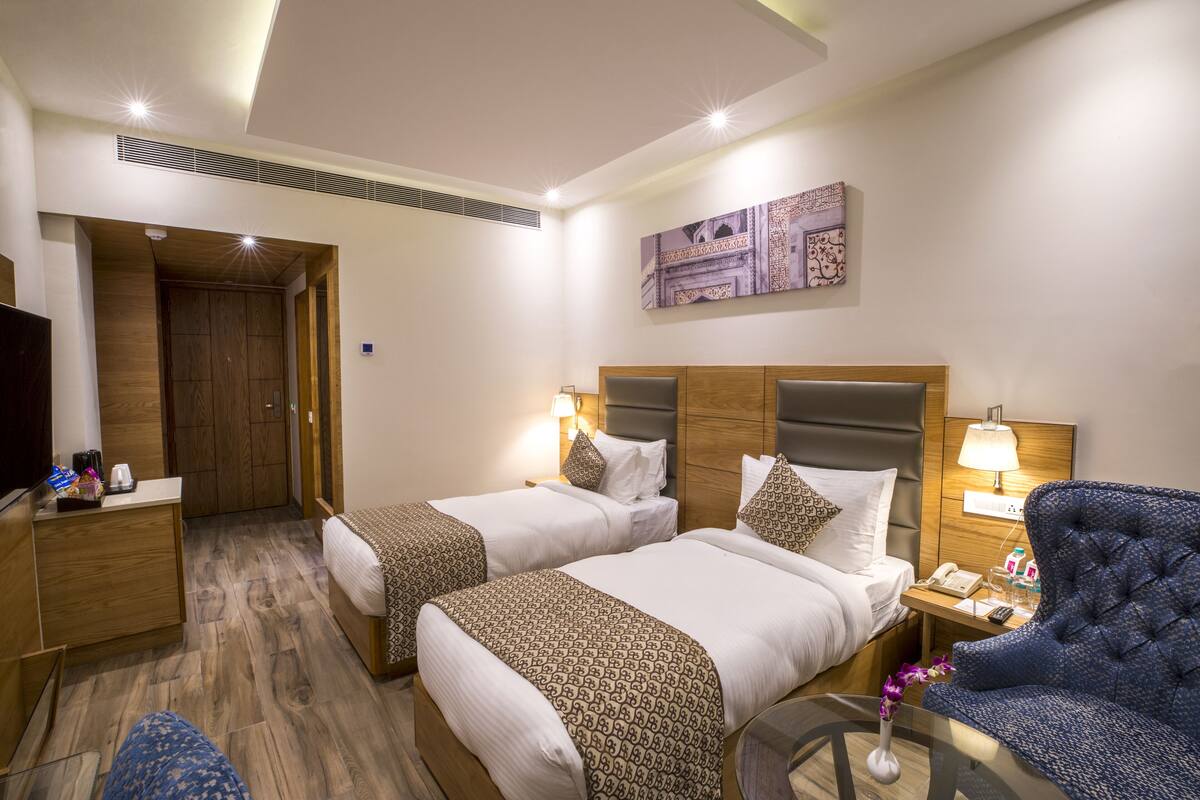 A hotel room with two beds, a desk, a chair, and a TV.
