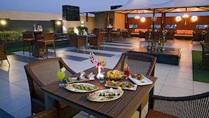 Un área de comedor al aire libre con mesas y sillas, una variedad de platos y una puesta de sol al fondo.