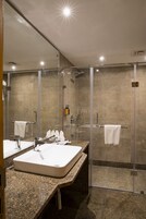 Un baño moderno con un lavamanos grande, cabina de ducha con mampara de vidrio y un espejo.
