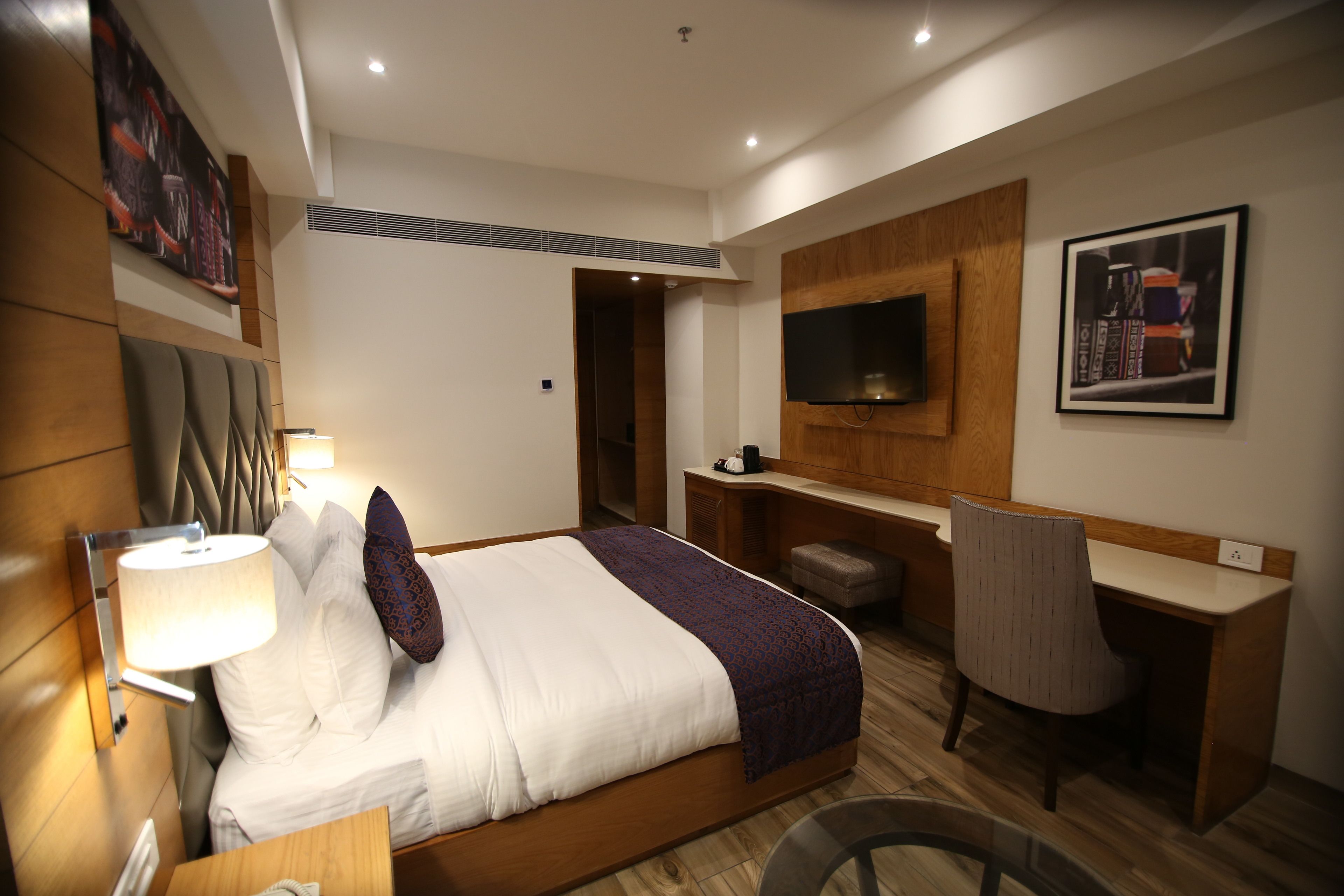 A modern hotel room with a large bed, a desk, a TV, and a seating area.