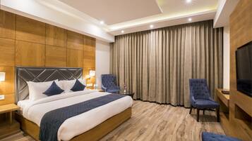 Habitación de hotel moderna con una cama grande, dos sillones, un televisor y piso de madera.