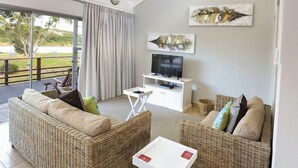 A modern living room with wicker furniture, a flat-screen TV, and artwork on the wall. - Addo River-View Lodge (Colchester)