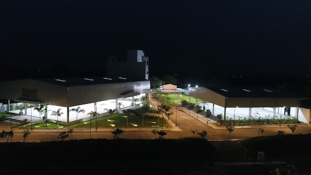 Un edificio moderno con techo plano y ventanas amplias, rodeado de un jardín bien iluminado con palmeras.