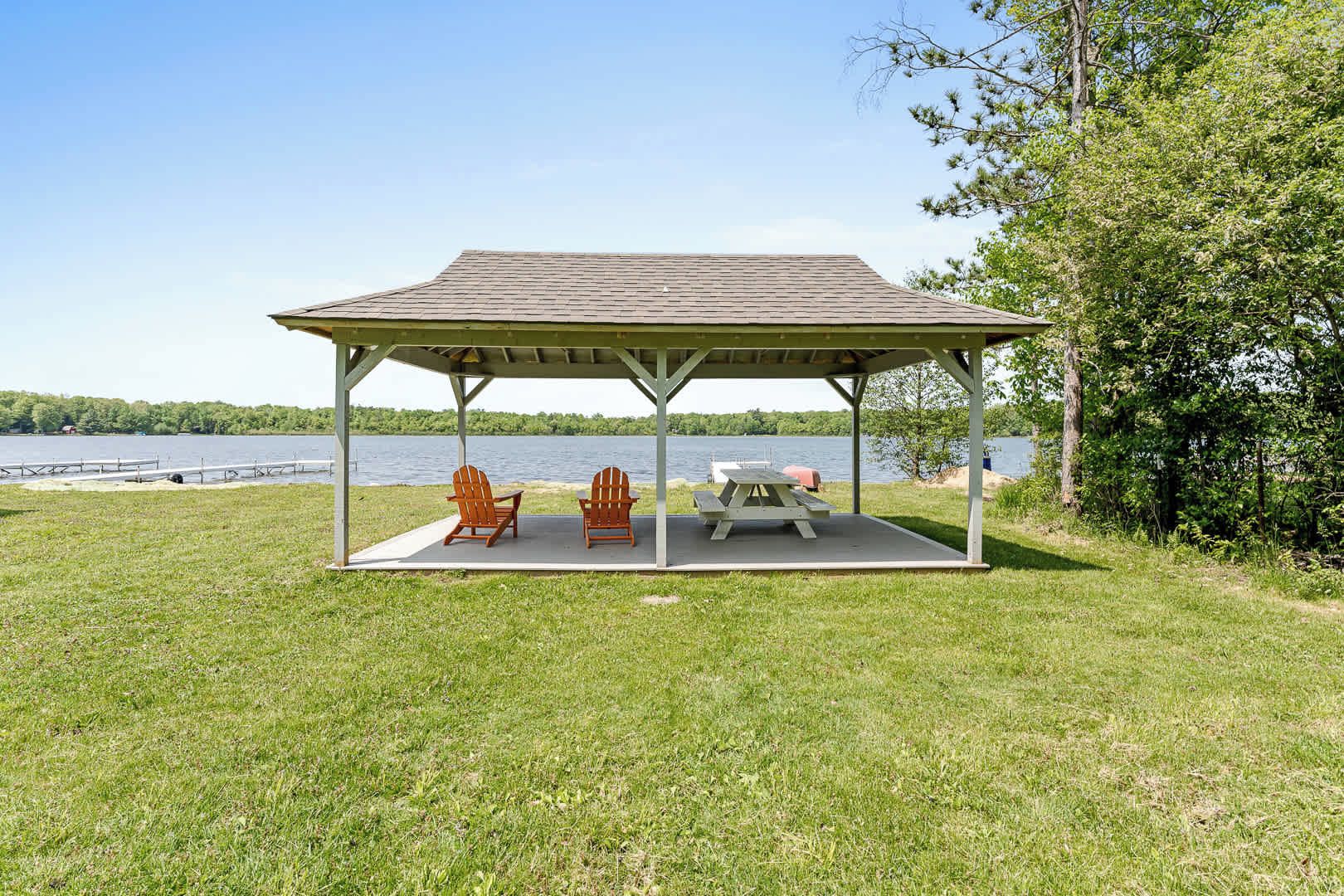 Et overdækket picnicområde med to Adirondack-stole og et picnicbord med udsigt over en sø.