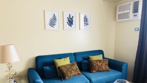 Un sofá azul con cojines estampados, una mesa de centro de vidrio con objetos decorativos e impresiones botánicas enmarcadas en la pared.