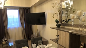 Un comedor de hotel con una mesa preparada para cuatro personas, un televisor de pantalla plana montado en la pared y un espejo decorativo sobre la mesa.