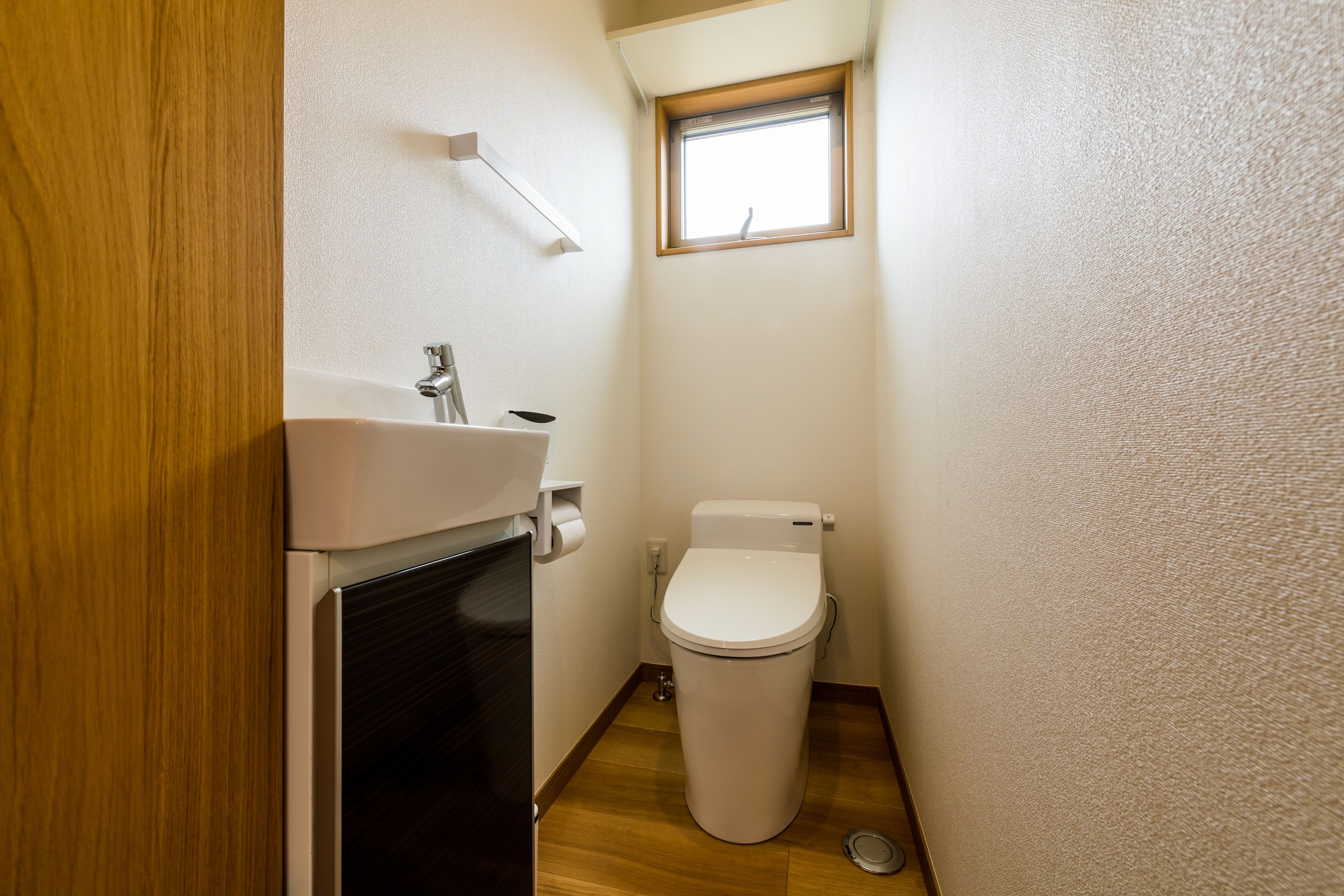 Une petite salle de bain avec des toilettes blanches, un lavabo et une fenêtre.