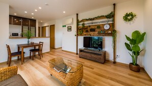 Ein modernes Wohnzimmer mit Holzboden, einem Glastisch, einem Fernseher und einem Kamin, über dem sich eine Uhr befindet.