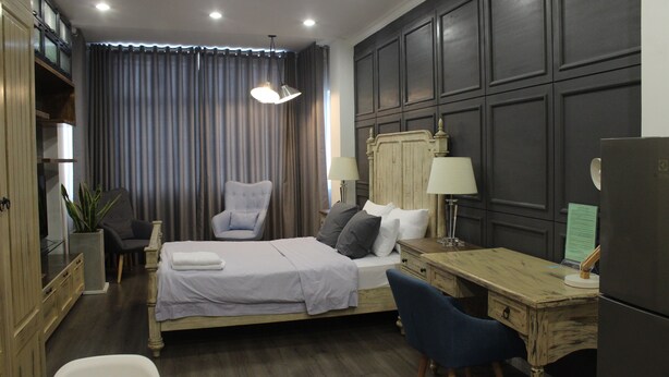 Une chambre à coucher comprenant un lit, deux tables de chevet avec des lampes, un bureau, une chaise, une armoire et une grande fenêtre avec des rideaux.