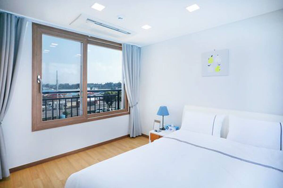 A hotel room with a large window, a bed, a nightstand, and a lamp.