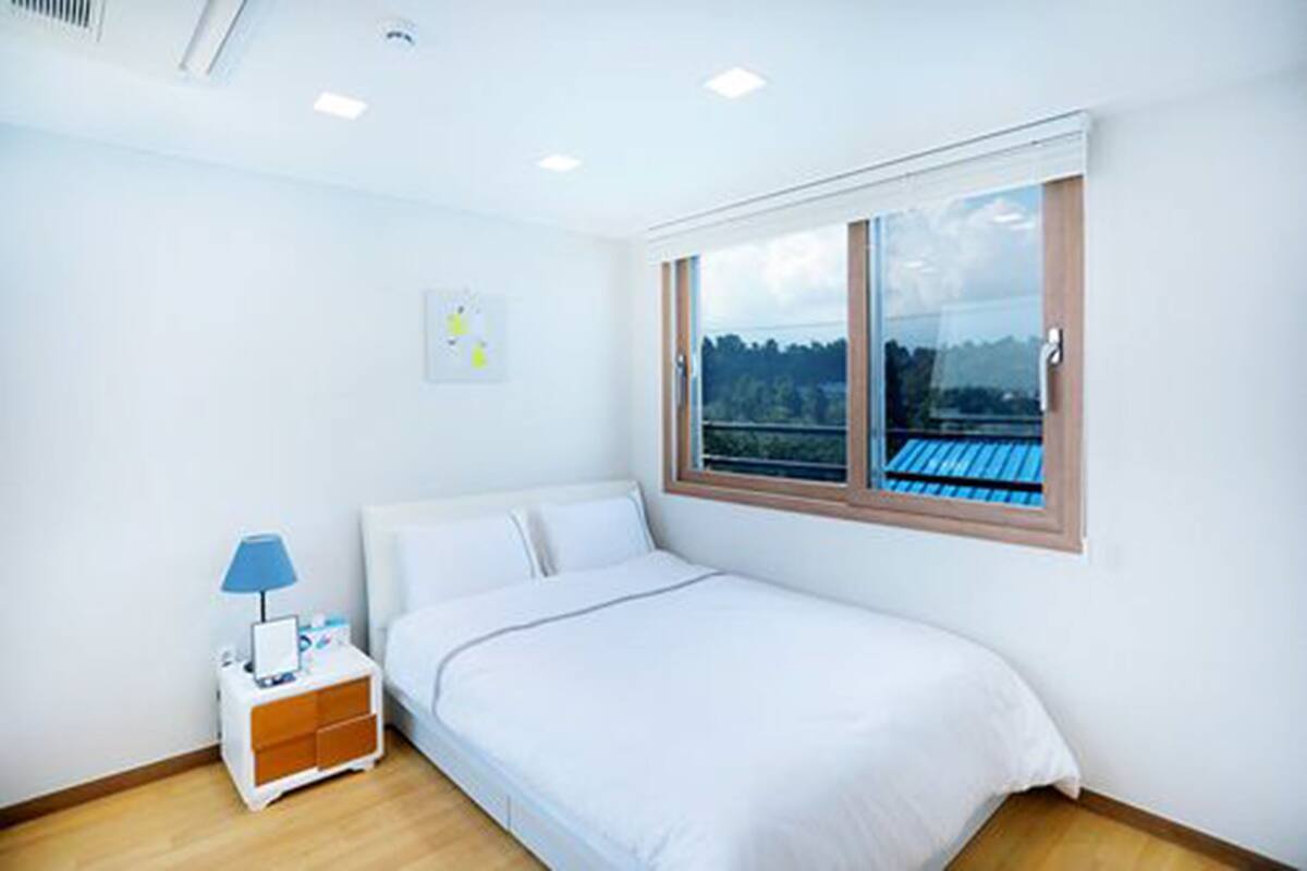A bedroom with a bed, a nightstand, a window with a view of the outdoors, and a ceiling light.