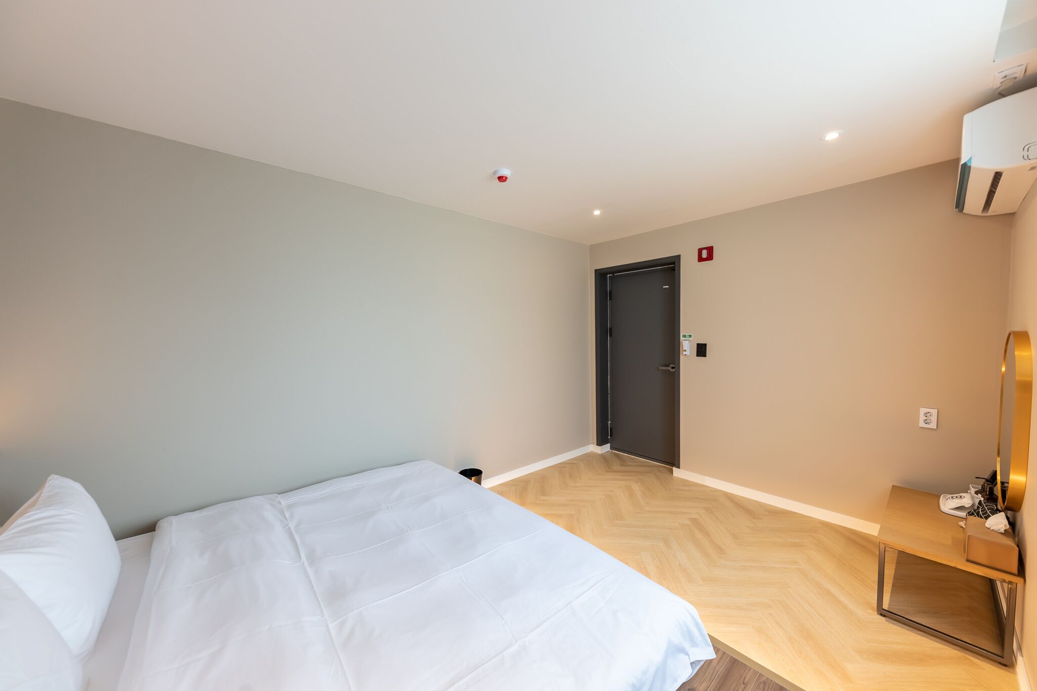A hotel room with a bed, a desk, a chair, and a door.
