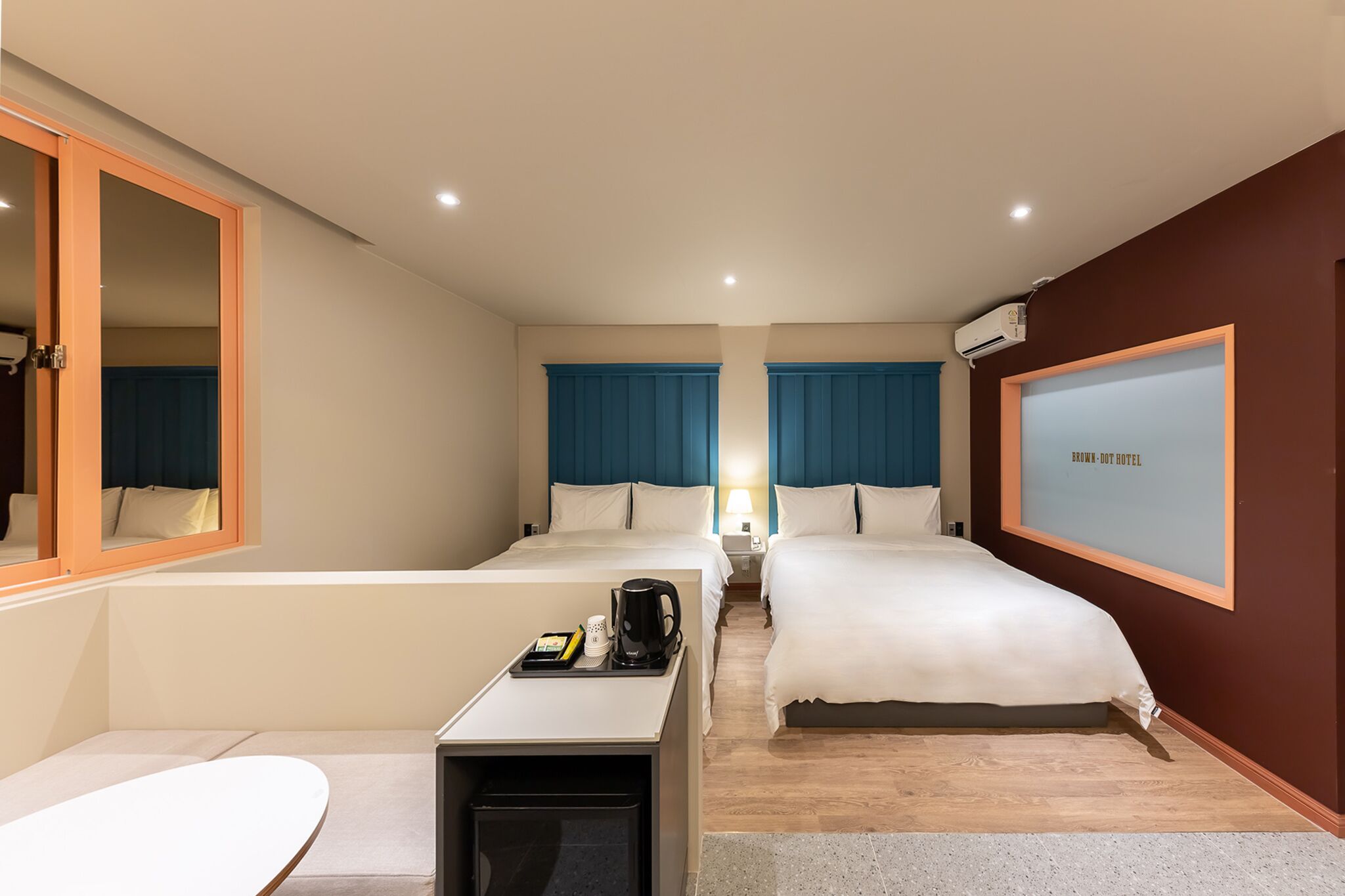A hotel room with two beds, a desk with a coffee maker, a TV, and a window with curtains.