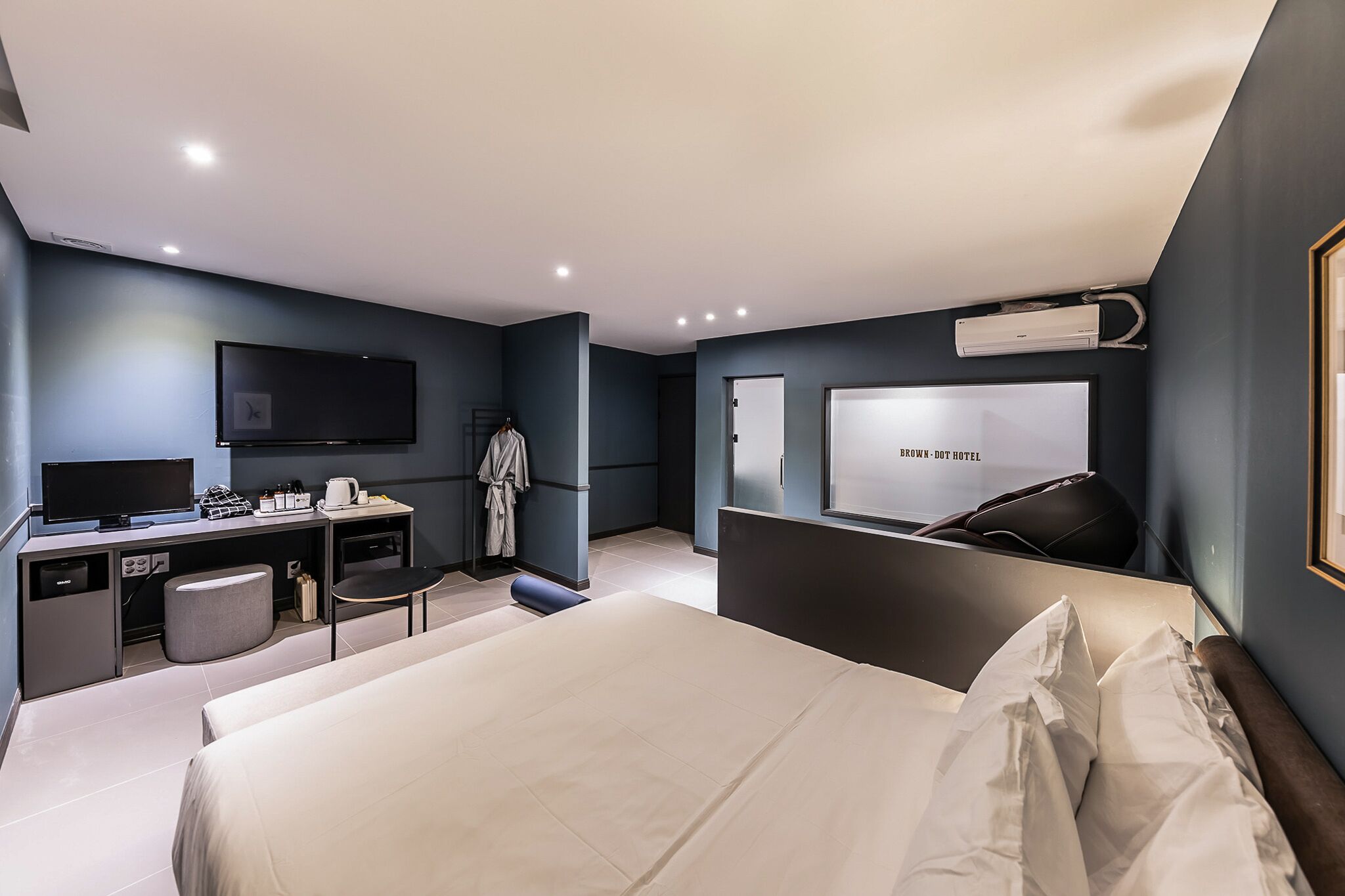 Et moderne hotelværelse med seng, skrivebord med fladskærms-tv, garderobe og et stort spejl.