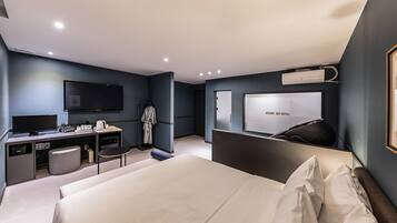 Et moderne hotelværelse med seng, skrivebord med fladskærms-tv, garderobe og et stort spejl.
