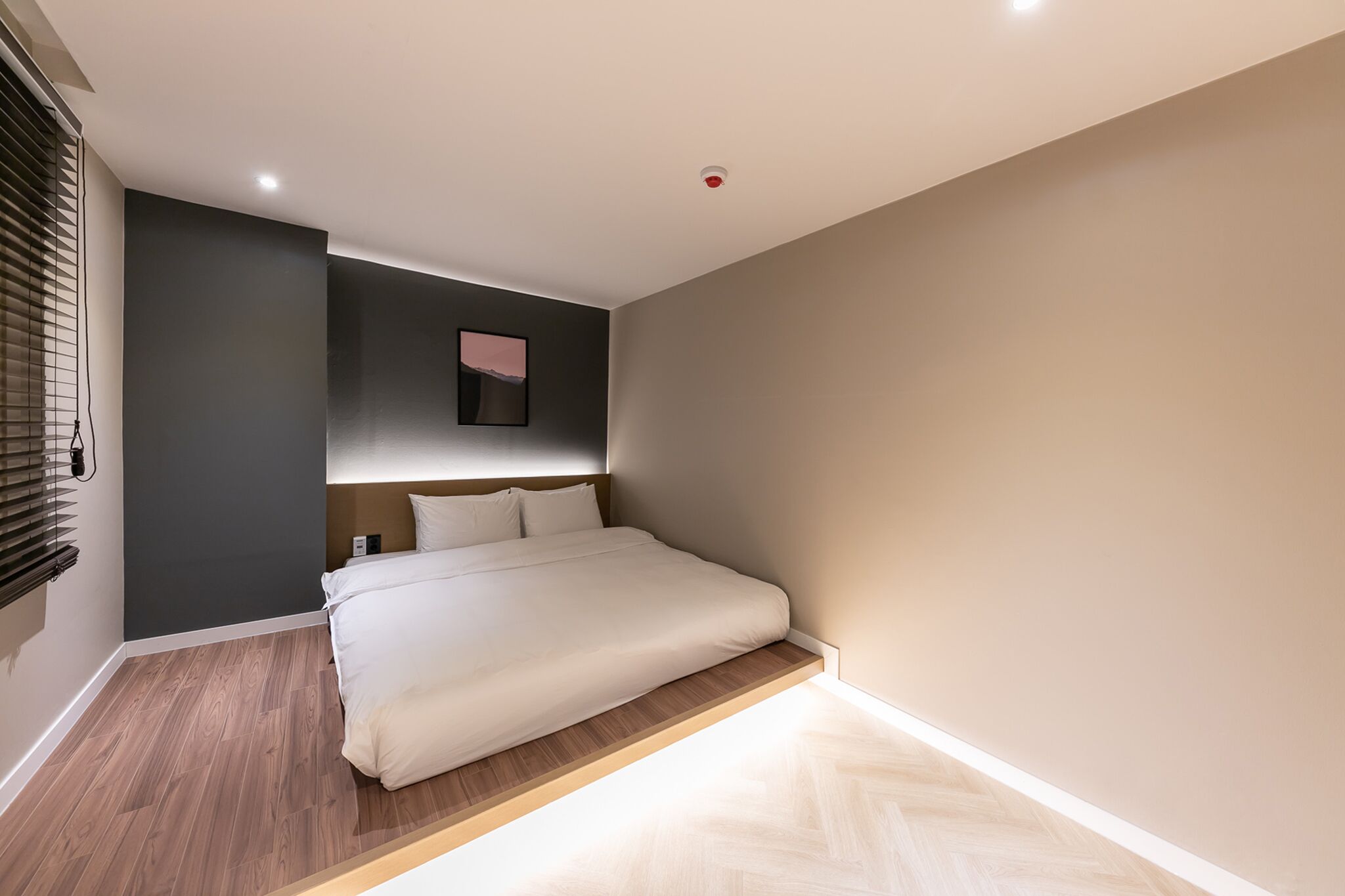 A modern bedroom with a bed, dark walls, a wooden floor, and a small picture on the wall.