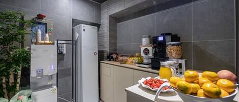 Una cocina moderna con refrigerador, cafetera y un cuenco de fruta.