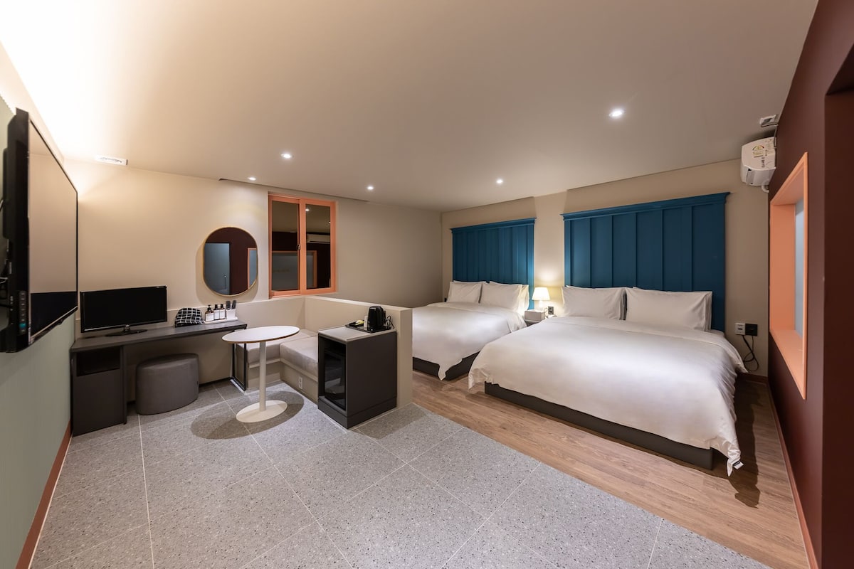 A hotel room with two beds, a desk, a chair, a TV, and a small table.