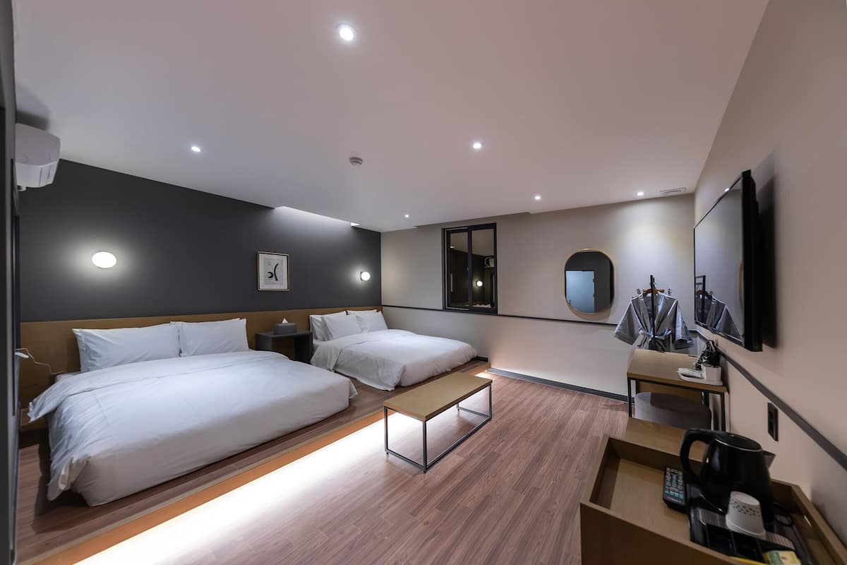 A modern hotel room with two single beds, a small desk with a coffee maker, a mirror, and a TV.