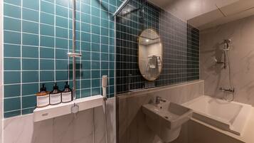 A modern bathroom with teal tiles, a large mirror, a bathtub, a shower, and three bottles of shampoo.