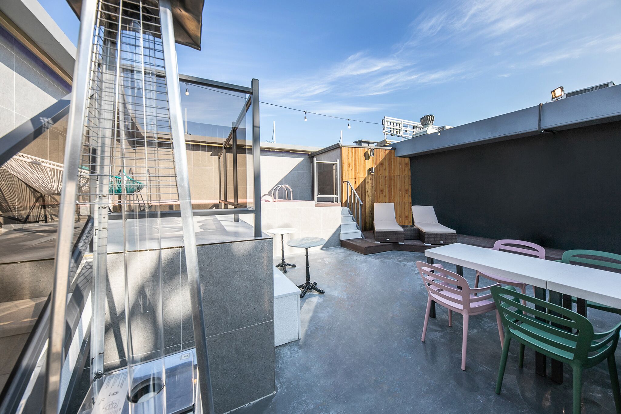 Una terraza en la azotea con barandilla de cristal, una mesa de comedor con sillas y vistas al horizonte de la ciudad.