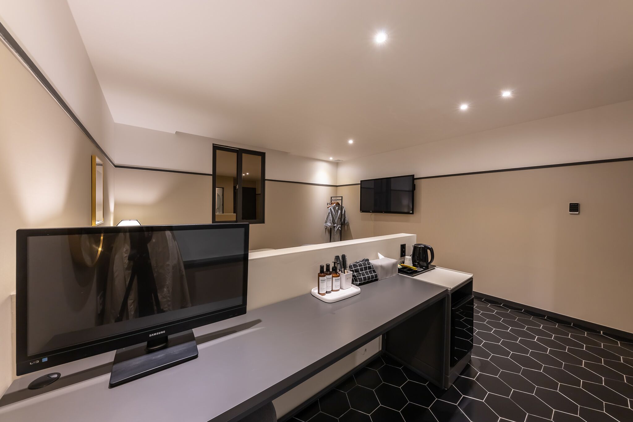 A modern hotel room with a flat-screen TV, a vanity with a mirror, and a black and white tiled floor.