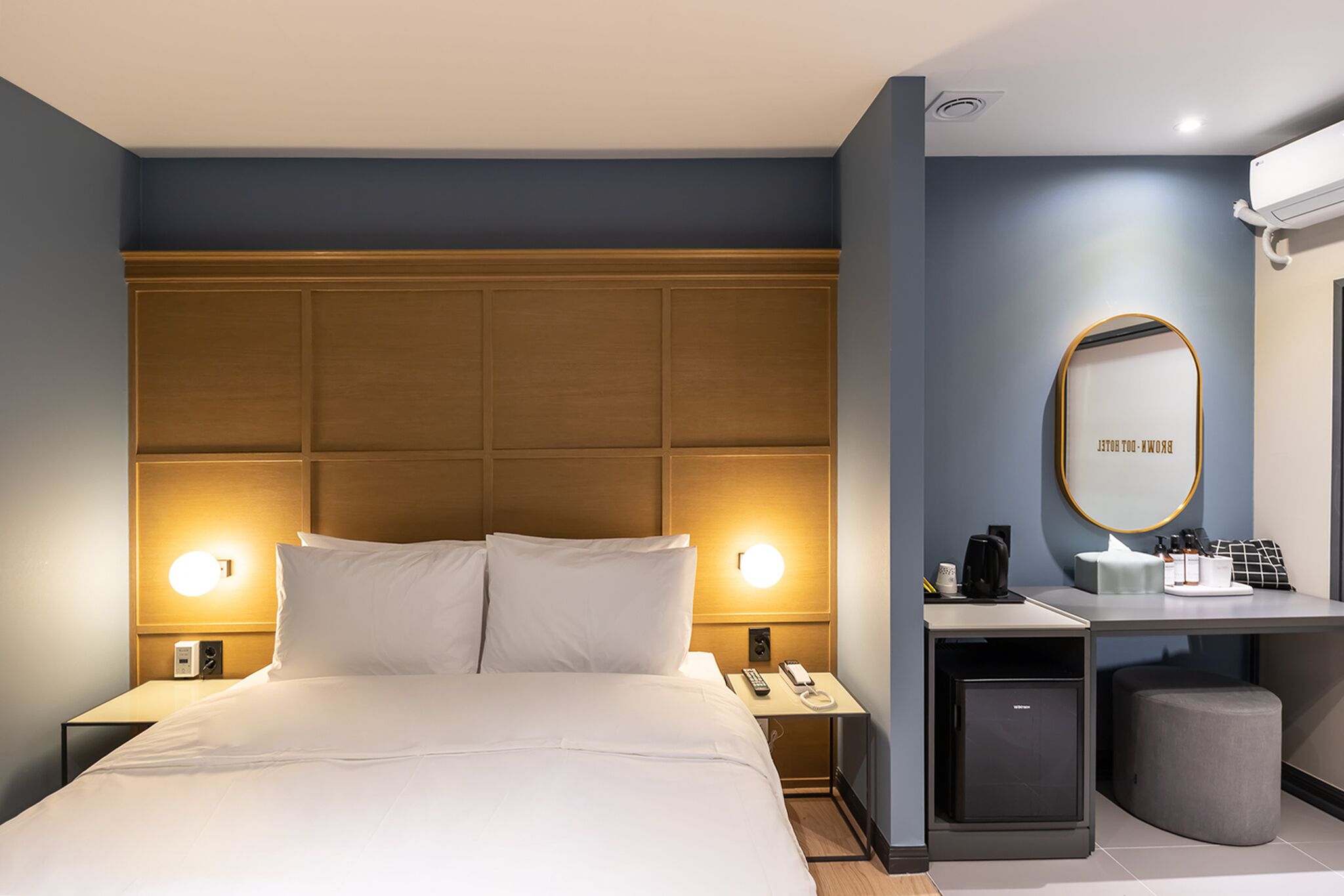 Habitación de hotel con una cama grande, lámparas de noche, un escritorio con espejo, un mueble pequeño y una mesita de noche con cafetera.