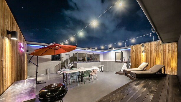 An outdoor patio area with a wooden deck, a barbecue grill, a table with chairs, and a lounge chair.