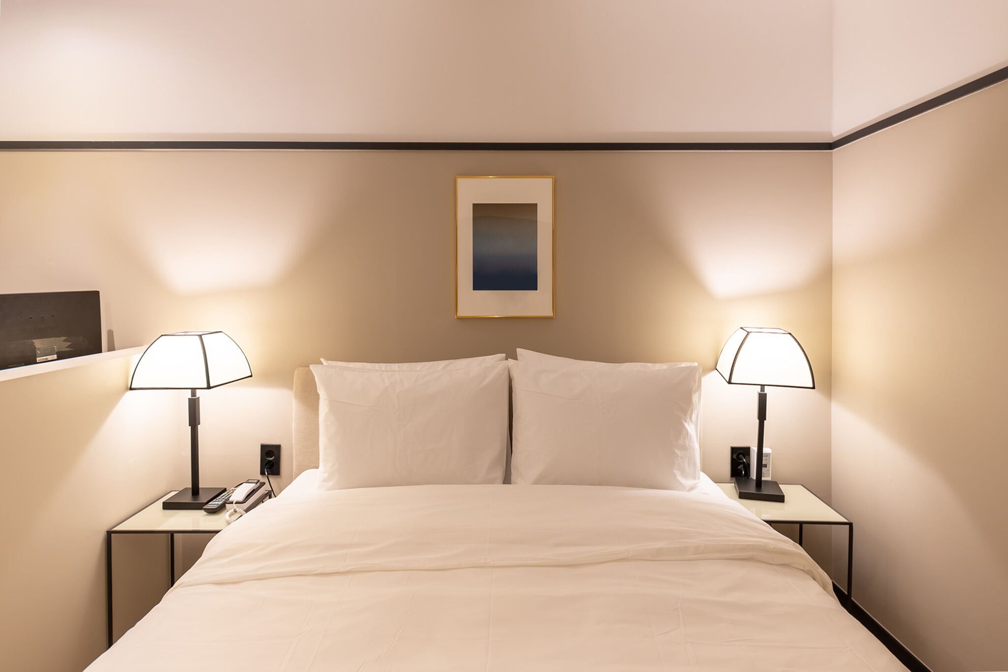 A hotel room with a bed, two bedside tables, lamps, a framed picture on the wall, and a phone on one of the tables.