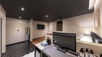 Habitación de hotel moderna con televisión de pantalla plana, escritorio con ordenador y zona de estar con sofá y lámparas.